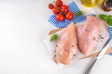 Mutfak masasında çiğ tavuk göğsü filetosu ve baharatlar. Beyaz yağsız et pişirme arka planı, beyaz masa kopyalama alanı