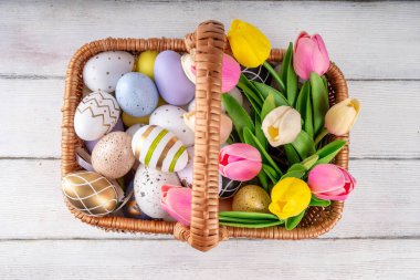 Paskalya boyalı geleneksel yumurtalar, lale çiçekleri sepetin içinde beyaz ahşap arka planda. Paskalya tebrik kartı, yumurta avı aile eğlence festivali davetiyesi arka plan fotokopi alanı
