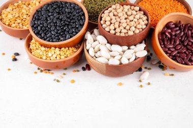 Çeşitli kuru fasulyeler, mercimek, mung, nohut, ahşap kaselerde bezelye çeşitleri. Legumes beyaz masa üst görünümünde. Vegan protein kaynakları yiyecek, kopyalama alanı