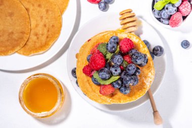 Healthy summer morning breakfast pancakes with fresh berry. Stack of traditional pancakes with blueberry, raspberries, honey. Healthy morning breakfast on white sunny background