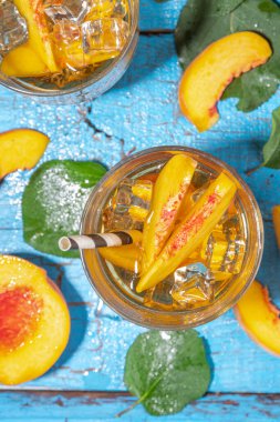 Homemade peach ice tea with ripe fresh peaches on high-colored blue wooden background