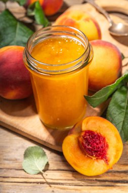 Red peach jam in small jar. Homemade autumn peach jam with fresh fruits. Fall preparations and canning on wooden table background copy space