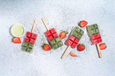 Dairy free green matcha and strawbery popsicles. Vegan ice cream popsicles with green matcha tea powder and dresh strawberry juice, Summer healthy organic dessert on white concrete background