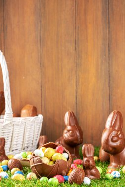 Easter egg hunting background. Various candy and chocolate Easter eggs, bunny and rabbits with basket for eggs on green grass park or garden background