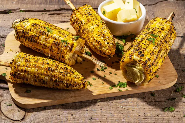 Sweet corn grilled with butter, cheese, cilantro and herbs. Vegetarian, healthy, clean eating barbeque food. Portioned bbq grill corn cobs on rustic wooden background