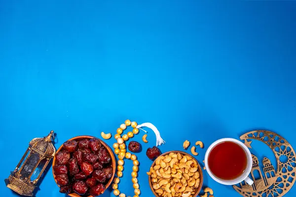 Ramadan muslim holiday background, with traditional treats - dates, nuts, dried fruits, sweets, religion rosary beads, lantern, tea, islamic Mosque, crescent moon Ramadan Kareem themed decorations