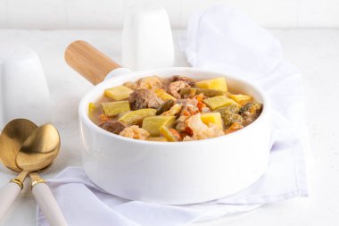 Sebze ve et güveci. Yürekli et ve sebze çorbası veya yahni, bahar sebzeli sığır burginyon, beyaz arka planda beyaz tencerede dengeli diyet yemeği.