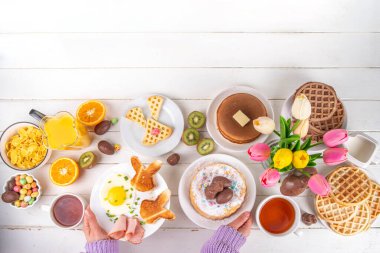 Paskalya tatili tatlı kahvaltı, brunch. Paskalya süslü Belçika waffle 'ları, krepler, kahvaltı gevrekleri ve süt, kızarmış yumurtalar kızarmış ekmek ve pastırma, Paskalya çikolatalı yumurtalar ve bahar çiçekleriyle birlikte tavşan.