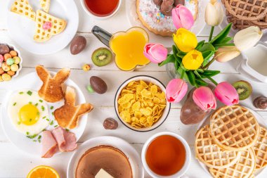 Paskalya tatili tatlı kahvaltı, brunch. Paskalya süslü Belçika waffle 'ları, krepler, kahvaltı gevrekleri ve süt, kızarmış yumurtalar kızarmış ekmek ve pastırma, Paskalya çikolatalı yumurtalar ve bahar çiçekleriyle birlikte tavşan.
