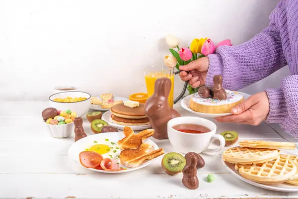 Paskalya tatili tatlı kahvaltı, brunch. Paskalya süslü Belçika waffle 'ları, krepler, kahvaltı gevrekleri ve süt, kızarmış yumurtalar kızarmış ekmek ve pastırma, Paskalya çikolatalı yumurtalar ve bahar çiçekleriyle birlikte tavşan.