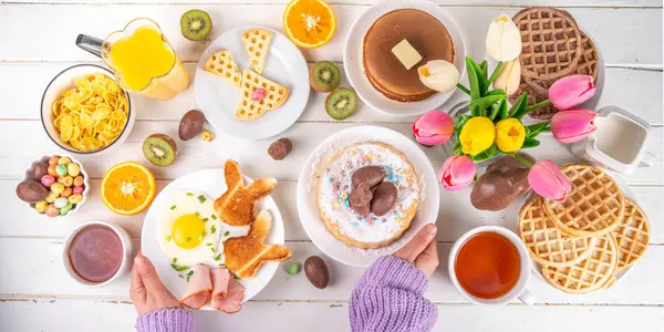 Paskalya tatili tatlı kahvaltı, brunch. Paskalya süslü Belçika waffle 'ları, krepler, kahvaltı gevrekleri ve süt, kızarmış yumurtalar kızarmış ekmek ve pastırma, Paskalya çikolatalı yumurtalar ve bahar çiçekleriyle birlikte tavşan.