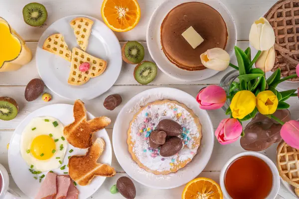 Paskalya tatili tatlı kahvaltı, brunch. Paskalya süslü Belçika waffle 'ları, krepler, kahvaltı gevrekleri ve süt, kızarmış yumurtalar kızarmış ekmek ve pastırma, Paskalya çikolatalı yumurtalar ve bahar çiçekleriyle birlikte tavşan.