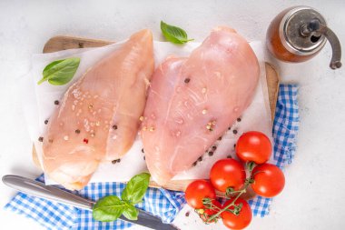 Mutfak masasında çiğ tavuk göğsü filetosu ve baharatlar. Beyaz yağsız et pişirme arka planı, beyaz masa kopyalama alanı
