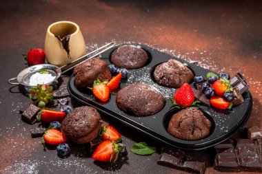 Çilekli çikolatalı kek. Kakao soslu ev yapımı çikolatalı kek tepsisi, şeker tozu ve taze çilek, yabanmersini, koyu kahverengi arka plan fotokopi alanı.