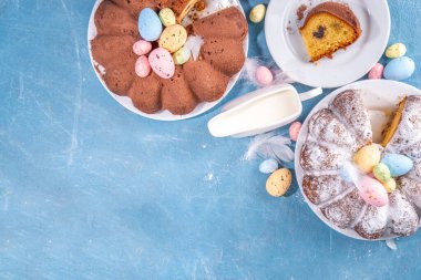 Traditional cake for Easter. Chocolate and vanilla Easter round cake with chocolate and sugar powder sprinkles, colorful Easter eggs, spring flowers, on a blue background copy space