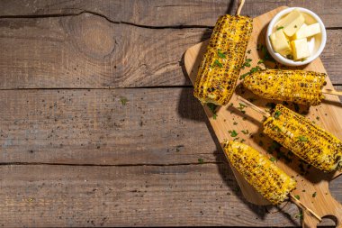 Sweet corn grilled with butter, cheese, cilantro and herbs. Vegetarian, healthy, clean eating barbeque food. Portioned bbq grill corn cobs on rustic wooden background