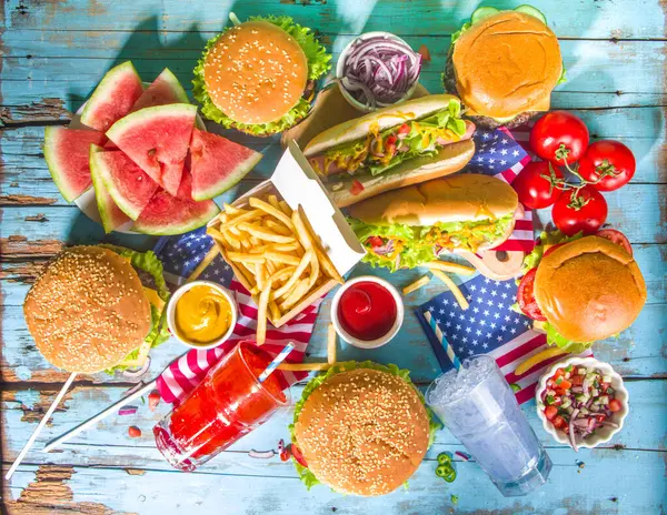 Fourth of July, Memorial Day, USA Independence Day concept. Patriotic, American traditional food. Picnic party with watermelon, burgers, hot dogs, drinks, blue wooden outdoor table background