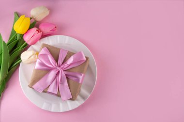 Anneler günü sofrası kurulumu. Pembe Anneler Günü 'nde kahvaltı, öğle yemeği, yemek menüsü, davetiye maketi. Altın çatal bıçak, tabak, lale çiçeği ve hediye kutusuyla güzel bir masa.