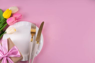 Anneler günü sofrası kurulumu. Pembe Anneler Günü 'nde kahvaltı, öğle yemeği, yemek menüsü, davetiye maketi. Altın çatal bıçak, tabak, lale çiçeği ve hediye kutusuyla güzel bir masa.