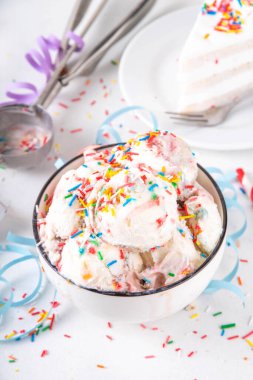Doğum günü pastası dondurması. Doğum günü pastasının kase porsiyonu renkli şekerli vanilyalı dondurma, masada doğum günü süslemeleri olan funfetti, fotokopi masası.