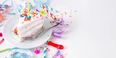 Doğum günü pastası dilimi, parti dekore masasında. Doğum günü pastası beyaz kremalı, şeker serpintili funfetti ve mum, kopyalama alanı