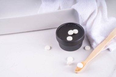 Diş fırçasında diş macunu hapları, beyaz katı diş macunu tableti bambu diş fırçası ve modern beyaz banyo arka planı.
