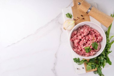 Yemek pişirme geçmişi. Çiğ taze kıyma, biftek, kuzu eti, beyaz mermer bir masada otlar, baharatlar ve soğanlar.