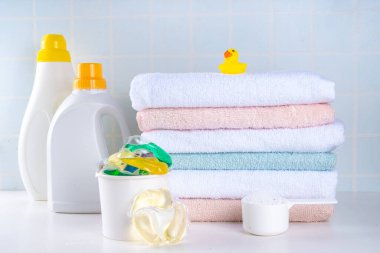 Çamaşır, çamaşır ve temizlik konsepti. Bir yığın temiz havlu, çeşitli deterjanlar - jeller, kapsüller, toz, çamaşır sepeti ve sevimli sarı ördek, beyaz banyo arka plan fotokopisi