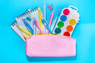 Back to school flatlay background. Pink pencil case with various school stationery on high-colored bright background
