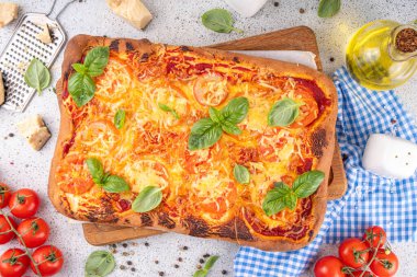 Domates ve fesleğenli ev yapımı margarita pizza, malzemeler ve arka planda beyaz mutfak masasında zeytinyağı.