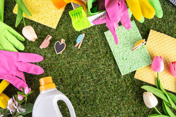 Весенняя уборка фона. Комплект чистящих средств, бутылок, аксессуаров и вещей с весенними цветами в корзине на белом деревянном зеленом саду