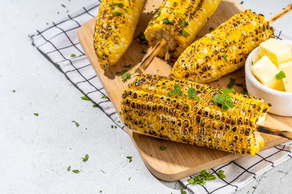 Sweet corn grilled with butter, cheese, cilantro and herbs. Vegetarian, healthy, clean eating barbeque food. Portioned bbq grill corn cobs on white background