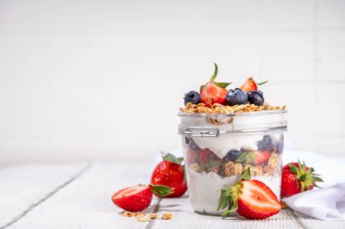 Yaz meyveleri kahvaltılık gevrek yoğurt katmanlı tatlı, yulaf taneli granola, çilek, ahşap masa arkasındaki yabanmersini fotokopi alanı.