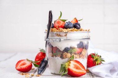 Yaz meyveleri kahvaltılık gevrek yoğurt katmanlı tatlı, yulaf taneli granola, çilek, ahşap masa arkasındaki yabanmersini fotokopi alanı.