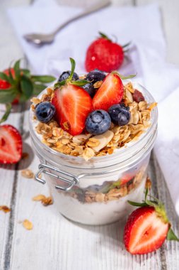 Yaz meyveleri kahvaltılık gevrek yoğurt katmanlı tatlı, yulaf taneli granola, çilek, ahşap masa arkasındaki yabanmersini fotokopi alanı.