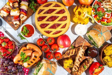 Çeşitli piknik barbekü yemekleri ve flatlay içiyorlar. Yaz bbq piknik yemekleri, ızgara etler, kebaplar, sebzeler, meyve salatası, geleneksel piknik pastası, sandviçler, üst görünüm fotokopi alanı.