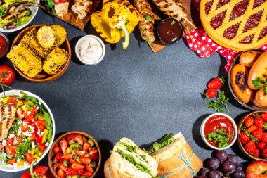 Çeşitli piknik barbekü yemekleri ve flatlay içiyorlar. Yaz bbq piknik yemekleri, ızgara etler, kebaplar, sebzeler, meyve salatası, geleneksel piknik pastası, sandviçler, üst görünüm fotokopi alanı.