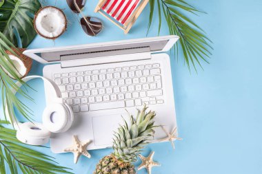 İş ve tatil. Yaratıcı yaz ofis dairesi beyaz dizüstü bilgisayarı, tropikal yaz aksesuarları, palmiye yaprakları, güneş gözlükleri, parmak arası terlikler, ananas ve açık mavi arka planda hindistan cevizi ile yatıyordu.