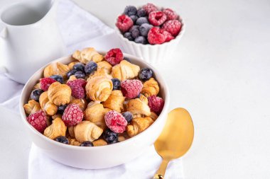 Küçük kahvaltılık kruvasan gevrekleri, taze böğürtlen ve süt. Fırında taze, ahududu ve yaban mersinli mini ay çöreği ile porsiyonlar, tatlı sabah atıştırması.