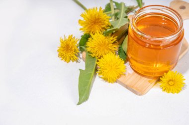 Karahindiba reçeli, kavanozda reçel ve beyaz bir masa arkasında taze karahindiba çiçekleri.