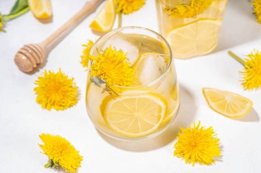 Karahindibalar soğuk buzlu çay ya da limonata. Çiçekli, karahindiba çiçeği içeceği. Çiçekler ve kökler, limon ve şurup. Arka planda beyaz masa fotokopi alanı.