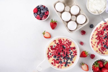 Fırında yoğurt pişirmek sağlıklı bir tatlı. Kadın el yapımı fırın Yunan yoğurt tatlısı taze donmuş böğürtlenlerle, beyaz mutfak masasında, malzemelerle, üst manzara