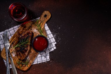 Grilled meat steak on dark table, Pork, veal, lamb, beef steak medium, medium well on cutting board, with spices, ketchup bbq sauce, wine glass. Dinner in steak restaurant menu, top view copy space