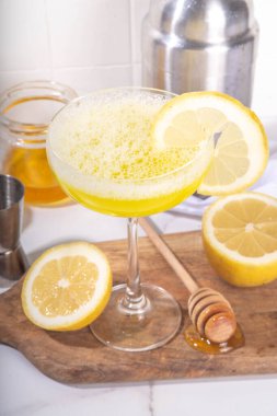 Tatlı ve ekşi alkol arısı dizleri kokteyli. Ev yapımı narenciye, bal arısı dizleri, malzemelerle birlikte beyaz arka planda sert ışık ve bar aletleriyle içerler.