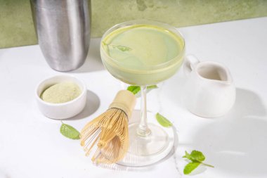 Kremalı matcha martini kokteyli Matchatini, modaya uygun soğuk yaz kokteyli. Alkolsüz kibrit mocktail ya da alkol kokteyli, martini bardaklarında yeşil kibrit tozu, arka planda sert ışık