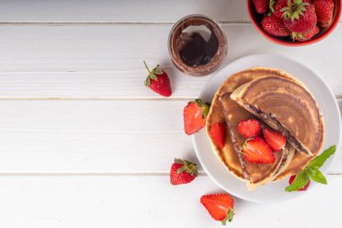 Fındıklı çikolatalı krep yığını. İçinde çikolata sosu olan tatlı kahvaltı krepleri ve beyaz mutfak masasında taze mercanlar.