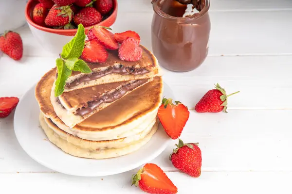 stock image Stack of chocolate nutella filled pancakes. Sweet breakfast pancakes with chocolate sauce inside it, and fresh stawberries, on white kitchen table