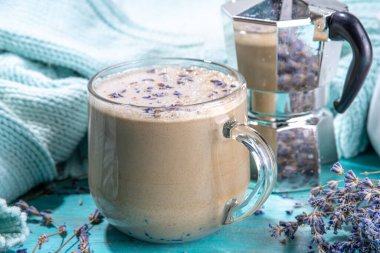 Bir fincan lavanta şuruplu cappuccino raf kahvesi. Aromatik lavandula mavi ahşap masa üzerinde sıcak kahve şişirilmiş