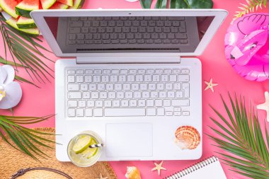 Yazlık ofis, çalışma geçmişi, blogcu iş yeri düzlüğü. Not defteri, hasır şapka, tropikal dekor ve yapraklarla dolu beyaz dizüstü bilgisayar klavyesi, açık pembe arka planda soğuk kokteyl bardağı.