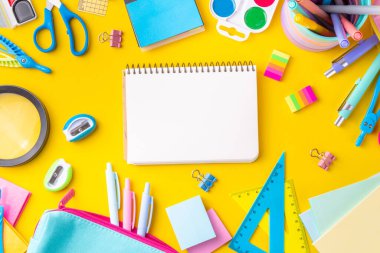 Okul ekipmanları parlak sarı düz yerde yatıyordu. Çeşitli okul ve ofis malzemeleri, aksesuarlar. Okul satışına geri dön. Üst görünüm kopyalama alanı